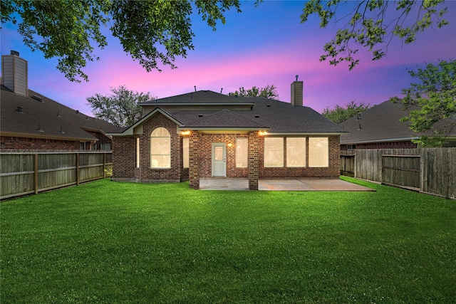 back of house at dusk with a lawn, a fenced backyard, and a patio area