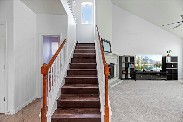 stairway featuring tile patterned flooring, ceiling fan, high vaulted ceiling, and a lit fireplace