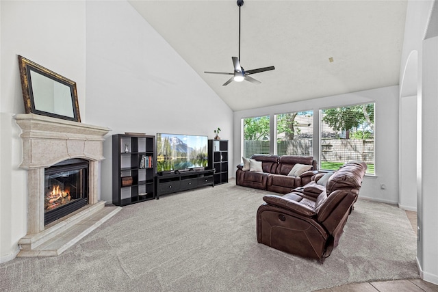 living room with carpet floors, a glass covered fireplace, baseboards, high vaulted ceiling, and a ceiling fan