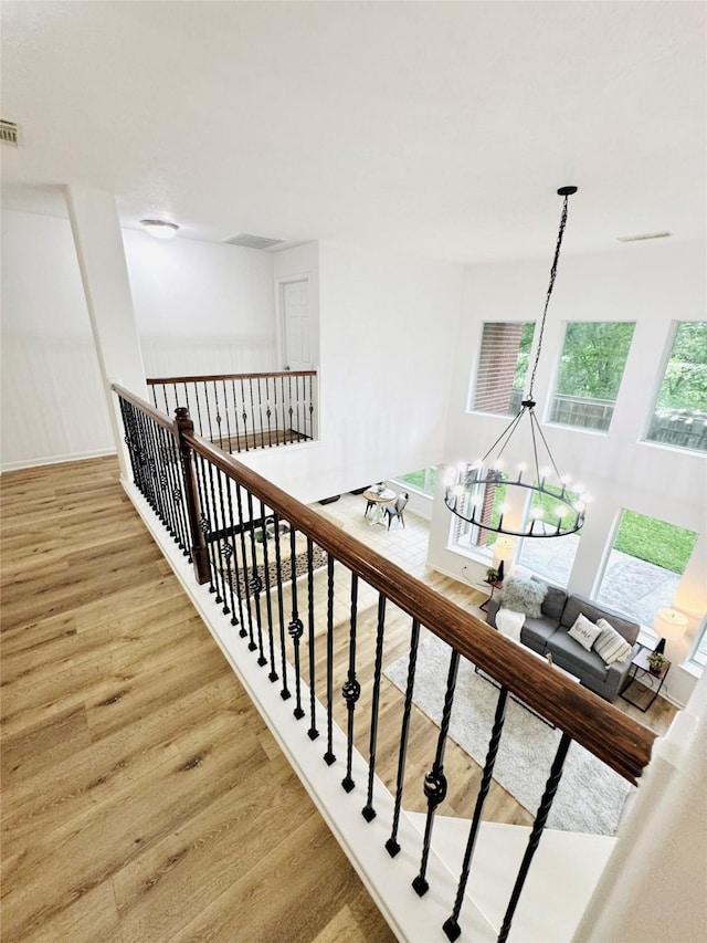 stairs featuring wood finished floors, a notable chandelier, and visible vents
