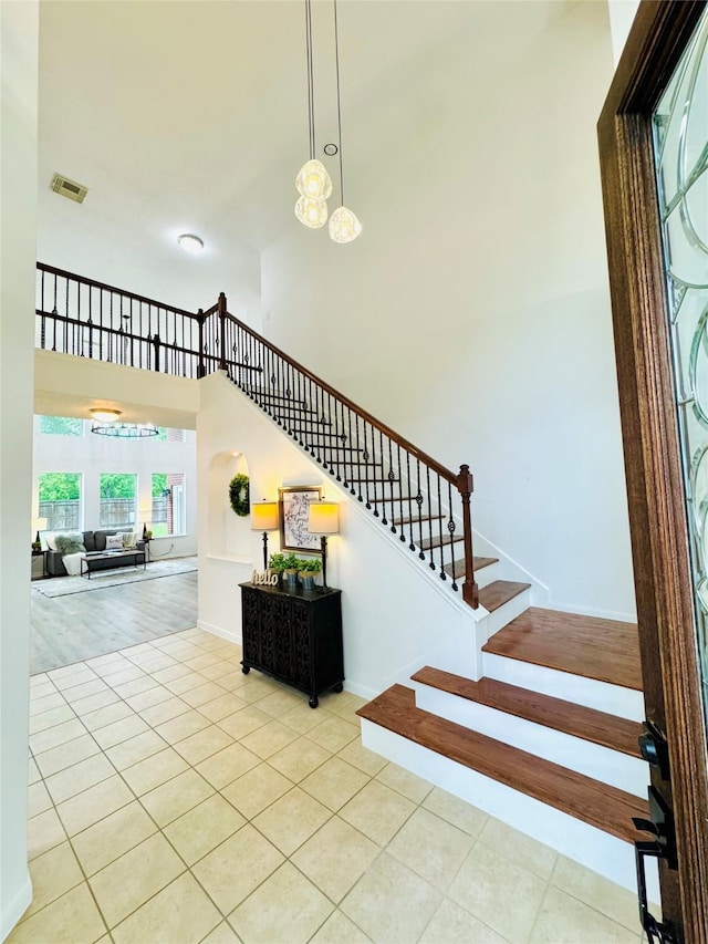 staircase featuring baseboards, a chandelier, tile patterned flooring, a high ceiling, and visible vents