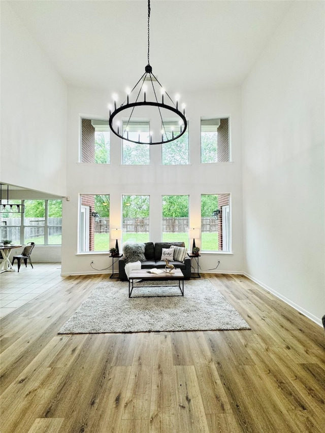 living area featuring a towering ceiling, a notable chandelier, baseboards, and wood finished floors