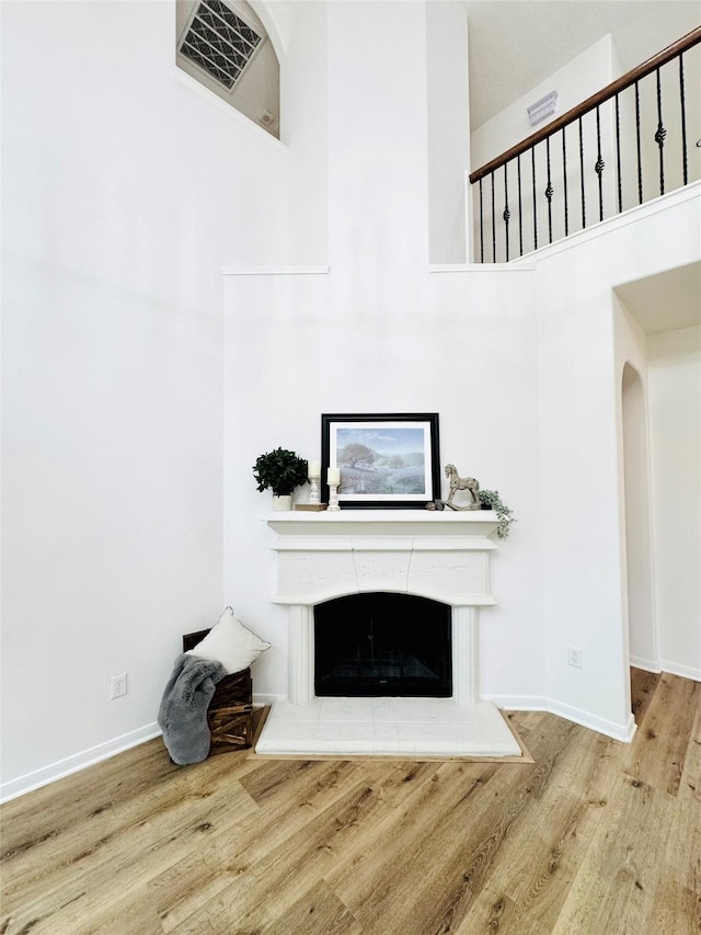 unfurnished living room with visible vents, a high ceiling, wood finished floors, a tiled fireplace, and baseboards