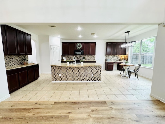 kitchen featuring tasteful backsplash, a sink, dark brown cabinets, black microwave, and light tile patterned flooring