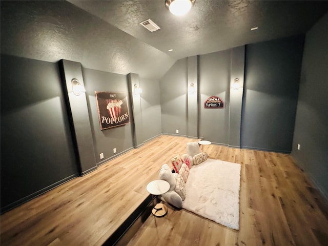 home theater room featuring visible vents, a textured ceiling, wood finished floors, and lofted ceiling