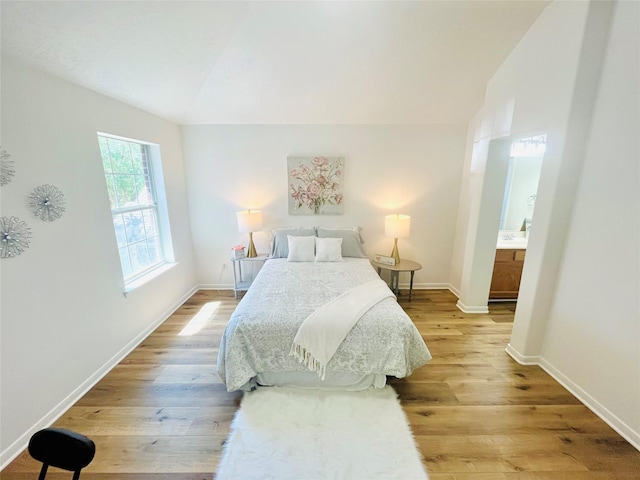 bedroom featuring light wood-type flooring, ensuite bathroom, baseboards, and lofted ceiling