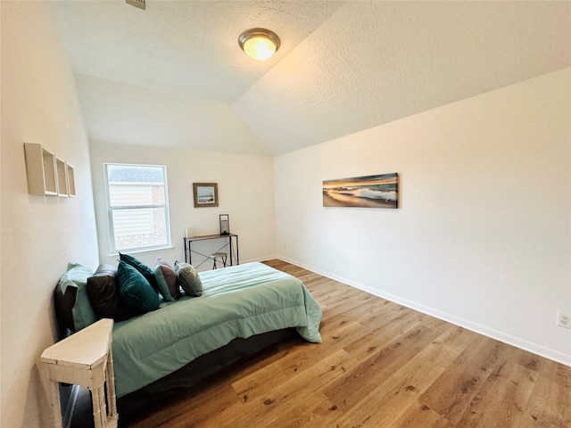 bedroom featuring a textured ceiling, baseboards, vaulted ceiling, and wood finished floors