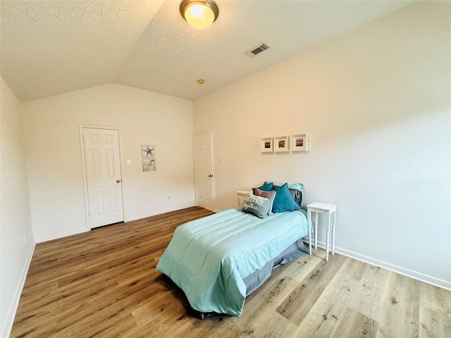 bedroom with baseboards, a textured ceiling, visible vents, lofted ceiling, and wood finished floors