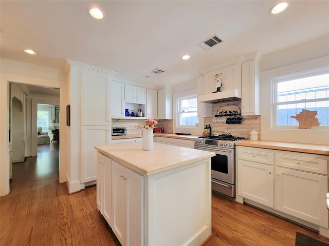 kitchen featuring visible vents, white cabinets, gas range, and ventilation hood