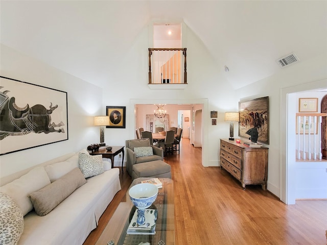 living area featuring high vaulted ceiling, light wood-type flooring, visible vents, a chandelier, and baseboards