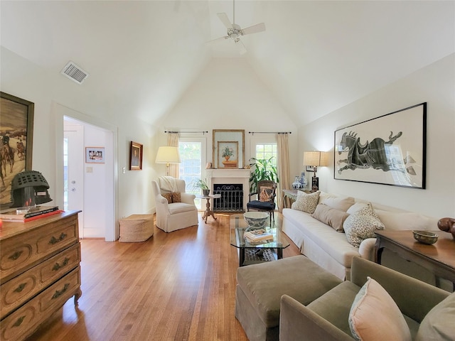 living room with a fireplace, light wood-style flooring, visible vents, ceiling fan, and high vaulted ceiling