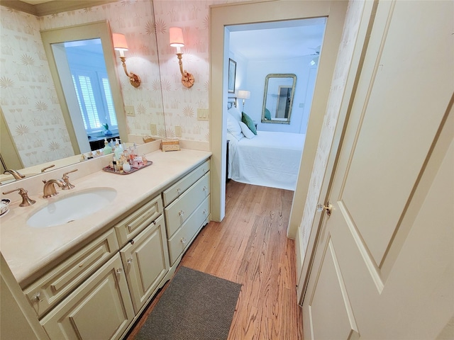ensuite bathroom with wallpapered walls, wood finished floors, vanity, and connected bathroom