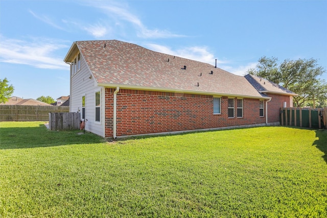 back of house with a yard, brick siding, fence, and a shingled roof