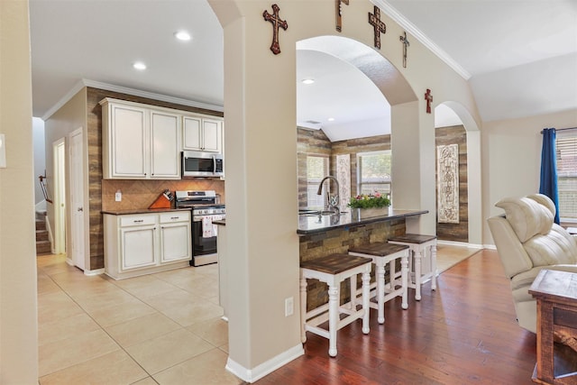 kitchen featuring a kitchen breakfast bar, arched walkways, ornamental molding, dark countertops, and stainless steel appliances