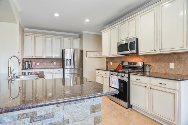 kitchen with a sink, cream cabinetry, appliances with stainless steel finishes, and dark stone counters