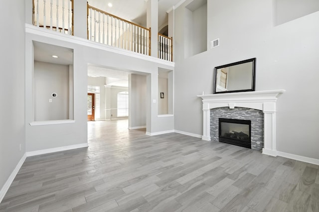 unfurnished living room featuring wood finished floors, baseboards, a fireplace, and a towering ceiling