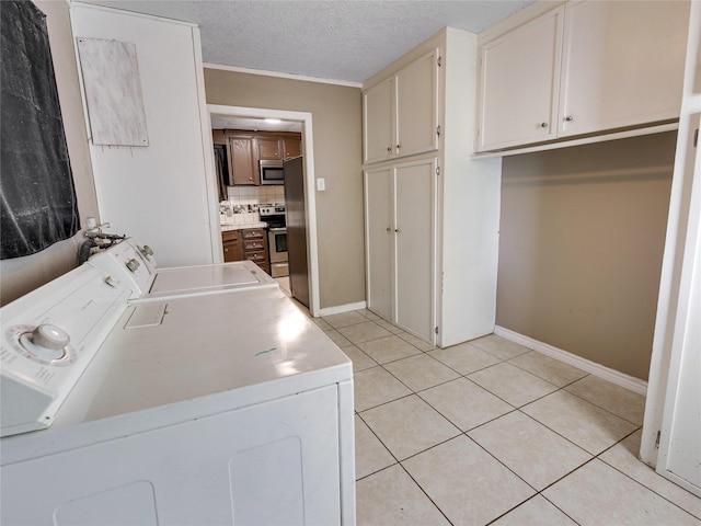 clothes washing area featuring baseboards, separate washer and dryer, a textured ceiling, cabinet space, and light tile patterned flooring