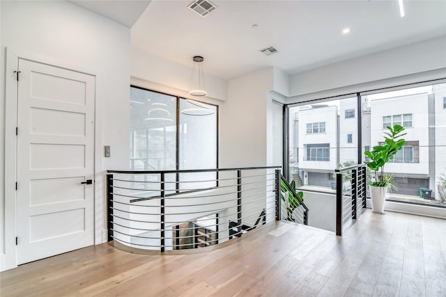 hallway with wood finished floors, visible vents, and an upstairs landing