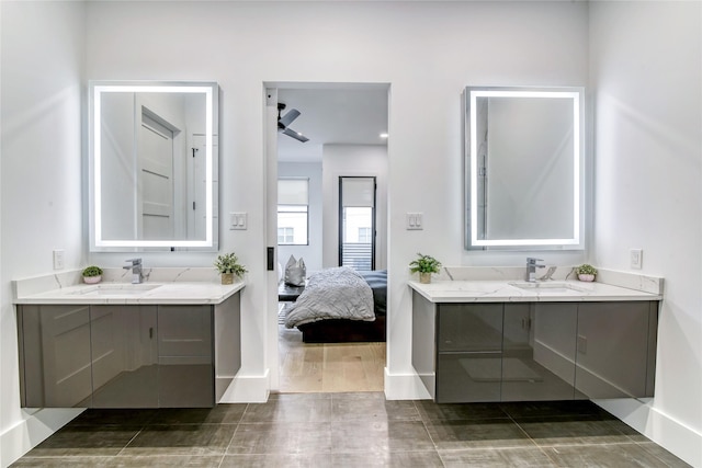 full bathroom featuring two vanities, ensuite bathroom, baseboards, and a sink
