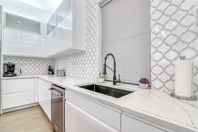 kitchen with modern cabinets, white cabinetry, light stone countertops, and a sink