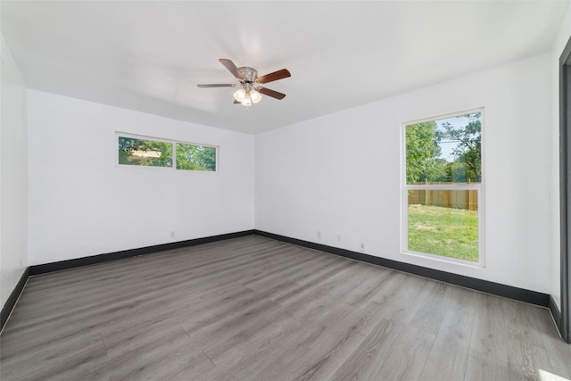 unfurnished room with ceiling fan, plenty of natural light, wood finished floors, and baseboards