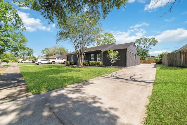 ranch-style house featuring concrete driveway, fence, and a front lawn