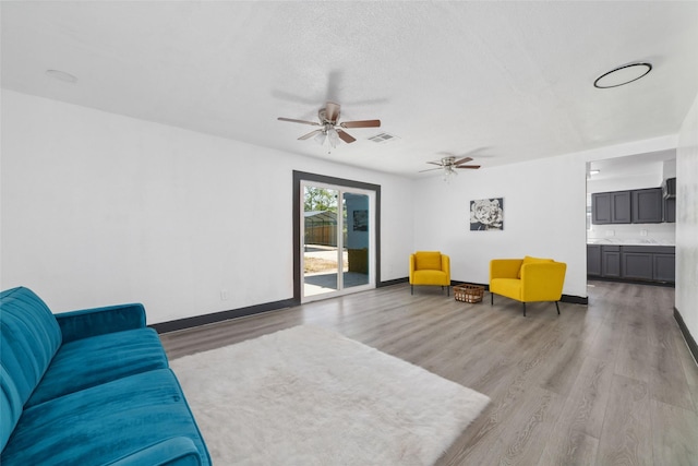 living area featuring wood finished floors, baseboards, a ceiling fan, and visible vents