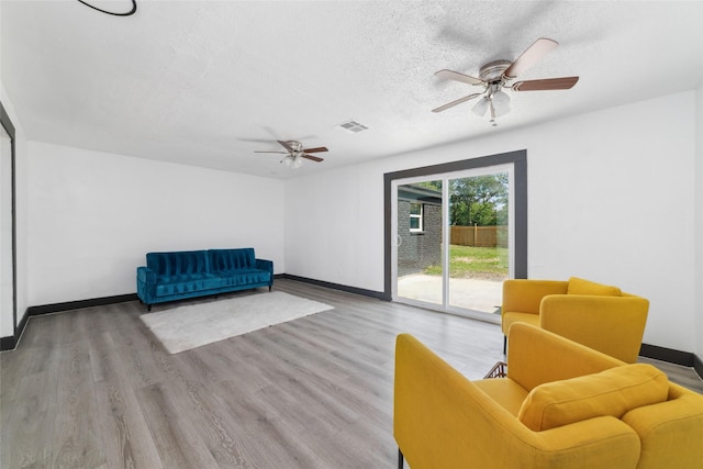 living area with visible vents, baseboards, a textured ceiling, and ceiling fan