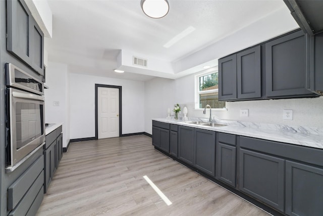 kitchen featuring a sink, stainless steel oven, light wood-style floors, and visible vents