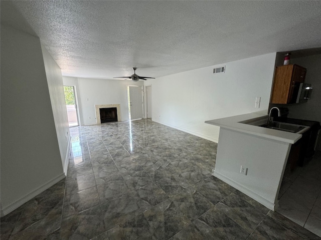 unfurnished living room featuring baseboards, a textured ceiling, visible vents, ceiling fan, and a sink