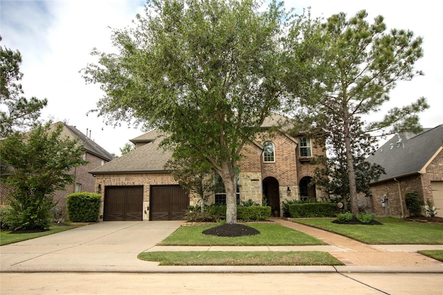 traditional-style home featuring an attached garage, stone siding, brick siding, a front lawn, and driveway