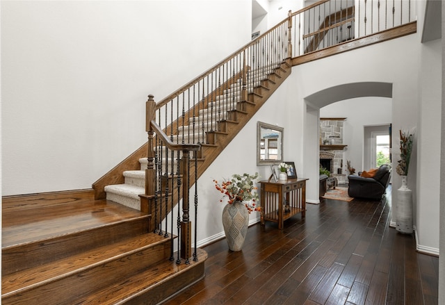 stairs featuring a fireplace, arched walkways, a towering ceiling, wood finished floors, and baseboards