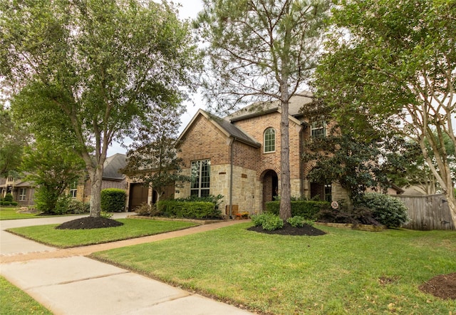 traditional-style house featuring concrete driveway, stone siding, a front lawn, brick siding, and fence