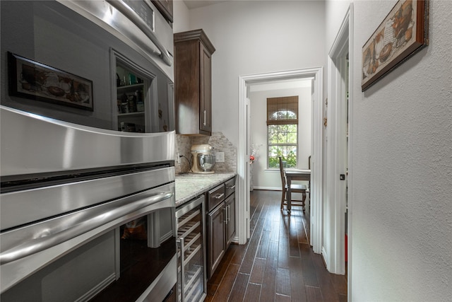 kitchen featuring light stone counters, backsplash, dark brown cabinets, dark wood finished floors, and beverage cooler