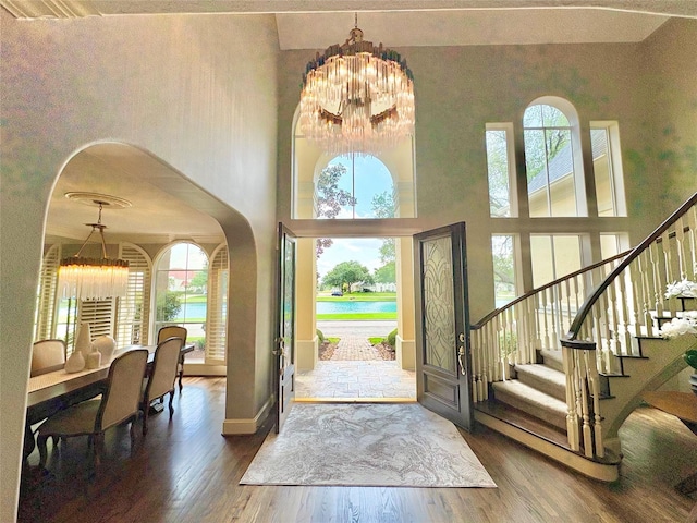 foyer featuring stairway, wood finished floors, a chandelier, a water view, and arched walkways
