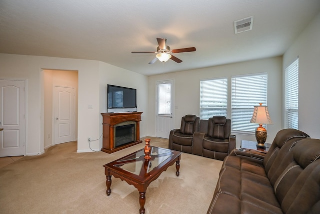 living room featuring visible vents, a fireplace, baseboards, light colored carpet, and a ceiling fan