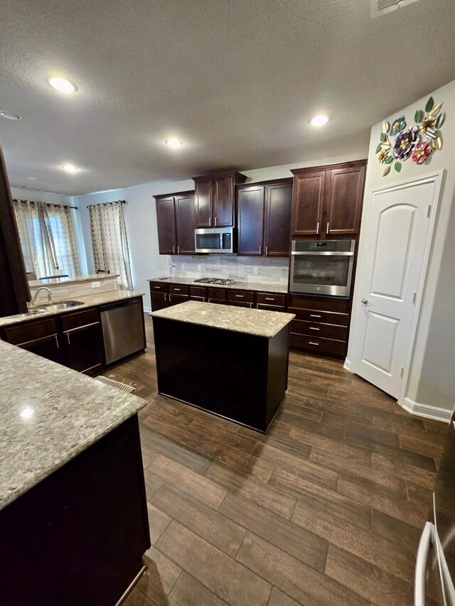 19003 Bene Vista Dr, Houston, TX 77084 - kitchen with appliances with stainless steel finishes, dark wood finished floors, backsplash, a center island, and dark brown cabinetry