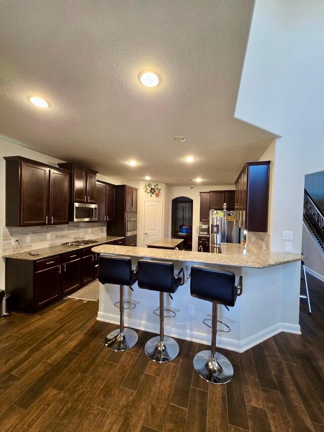 19003 Bene Vista Dr, Houston, TX 77084 - kitchen featuring appliances with stainless steel finishes, a kitchen bar, dark wood-type flooring, a peninsula, and recessed lighting