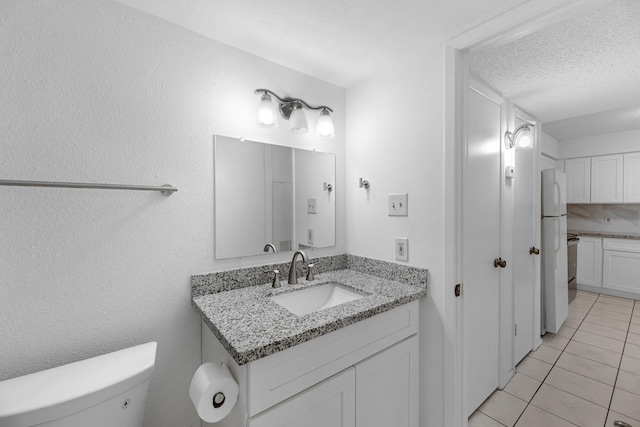 bathroom featuring toilet, a textured wall, a textured ceiling, vanity, and tile patterned floors