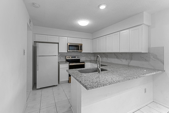 kitchen with a peninsula, a textured ceiling, white cabinetry, appliances with stainless steel finishes, and a sink
