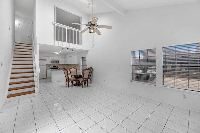 living area featuring light tile patterned floors, a ceiling fan, beamed ceiling, stairway, and a towering ceiling