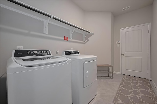 clothes washing area featuring light tile patterned floors, laundry area, washing machine and dryer, baseboards, and visible vents