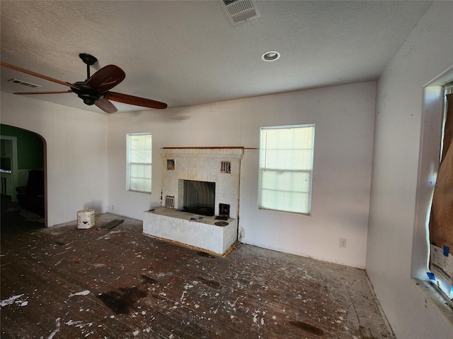 unfurnished living room featuring ceiling fan, a brick fireplace, a textured ceiling, and visible vents