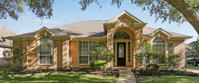 ranch-style home featuring roof with shingles and brick siding