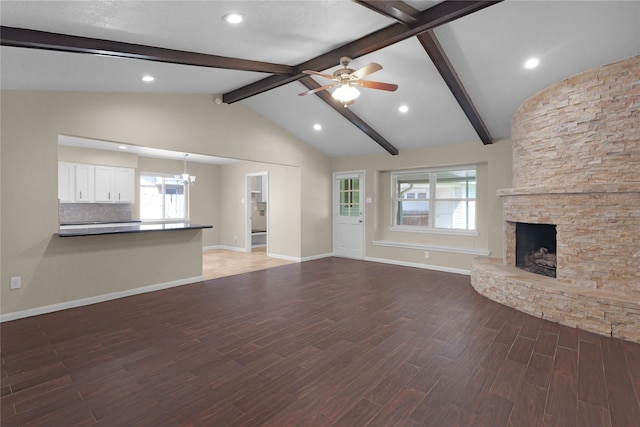 unfurnished living room with ceiling fan with notable chandelier, a fireplace, wood finished floors, vaulted ceiling with beams, and baseboards