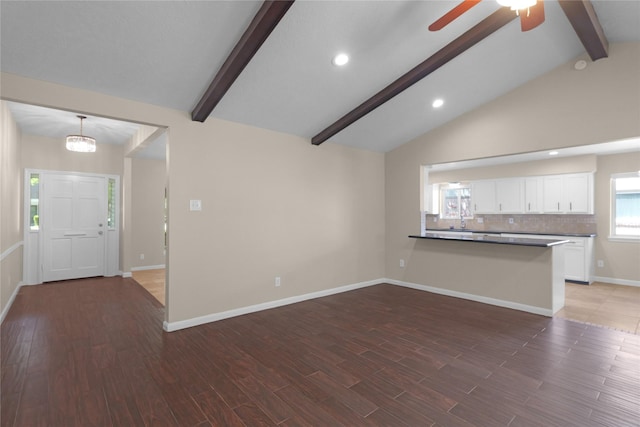 unfurnished living room with wood finished floors, baseboards, vaulted ceiling with beams, and ceiling fan