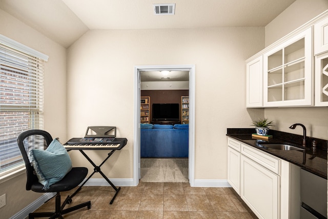 interior space with dark countertops, a sink, white cabinetry, visible vents, and glass insert cabinets