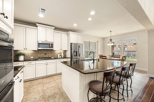 kitchen with a sink, a breakfast bar area, stainless steel appliances, backsplash, and a center island with sink
