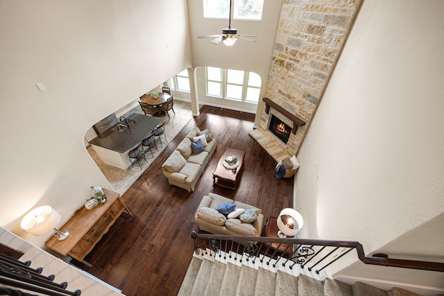 living room with a fireplace, a ceiling fan, hardwood / wood-style floors, and a towering ceiling
