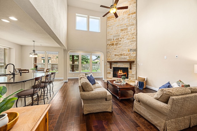 living room with dark wood-style flooring, a towering ceiling, a fireplace, baseboards, and ceiling fan
